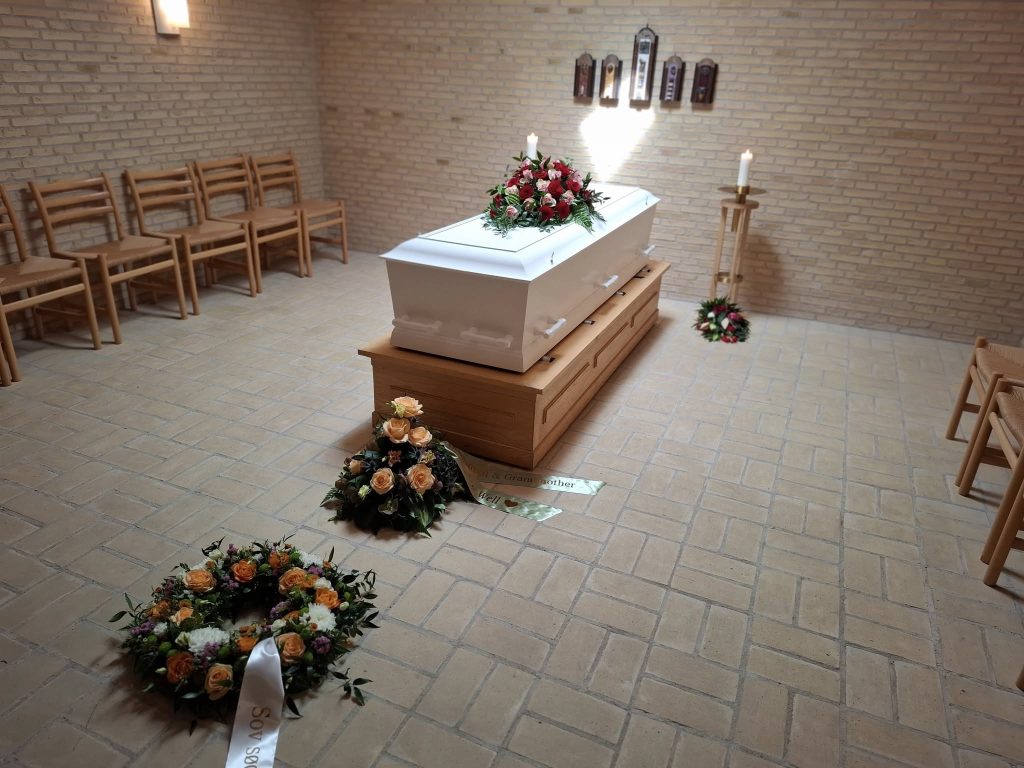 Bisættelse i kapel - Kiste med blomsterdekorationer sat op i kapel